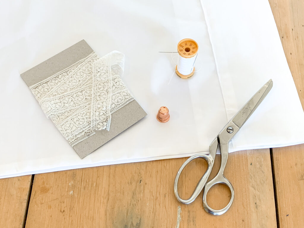 white lace sitting on a white pillow case with roll of white thread and rose gold thimble and dress makers scissors