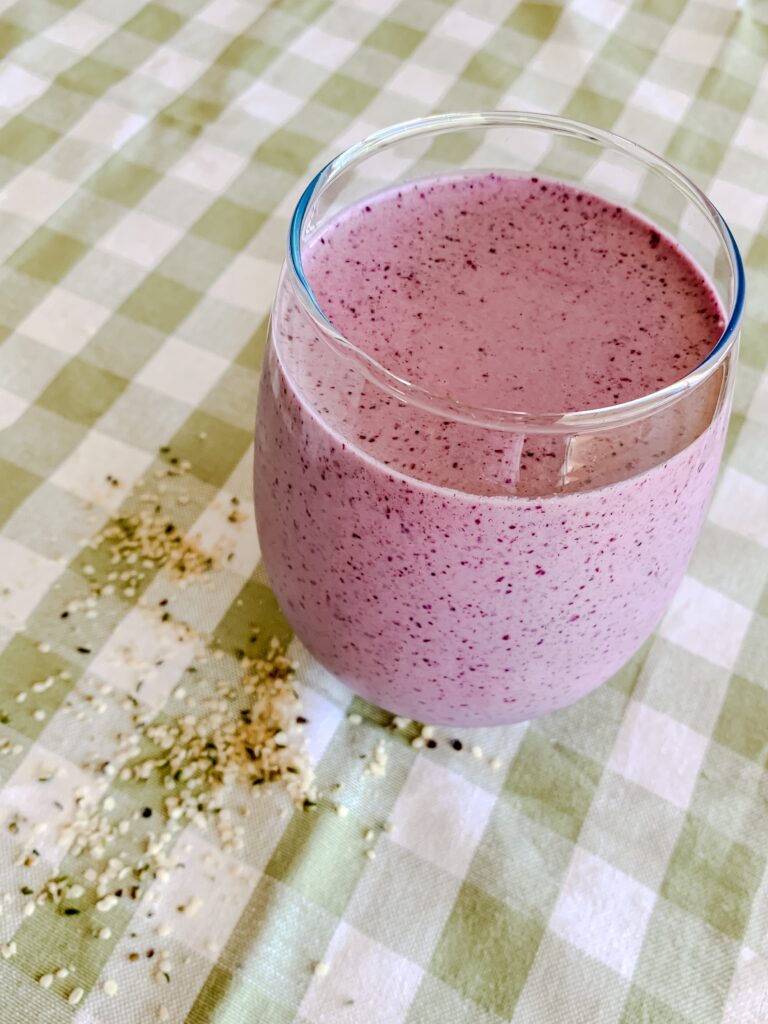 Energy Boosting Blueberry Smoothy in a glass on a green gingham cloth with hemp seeds sprinkled around 