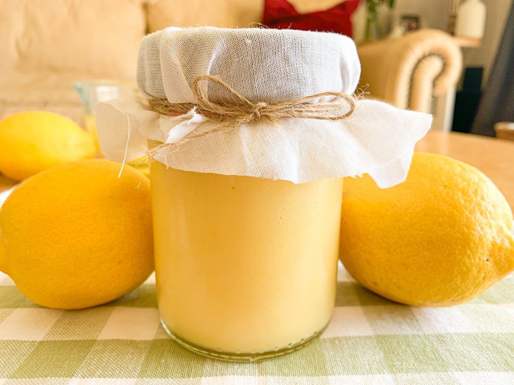 Bright yellow honey sweetened lemon butter in a jar surrounded by lemons